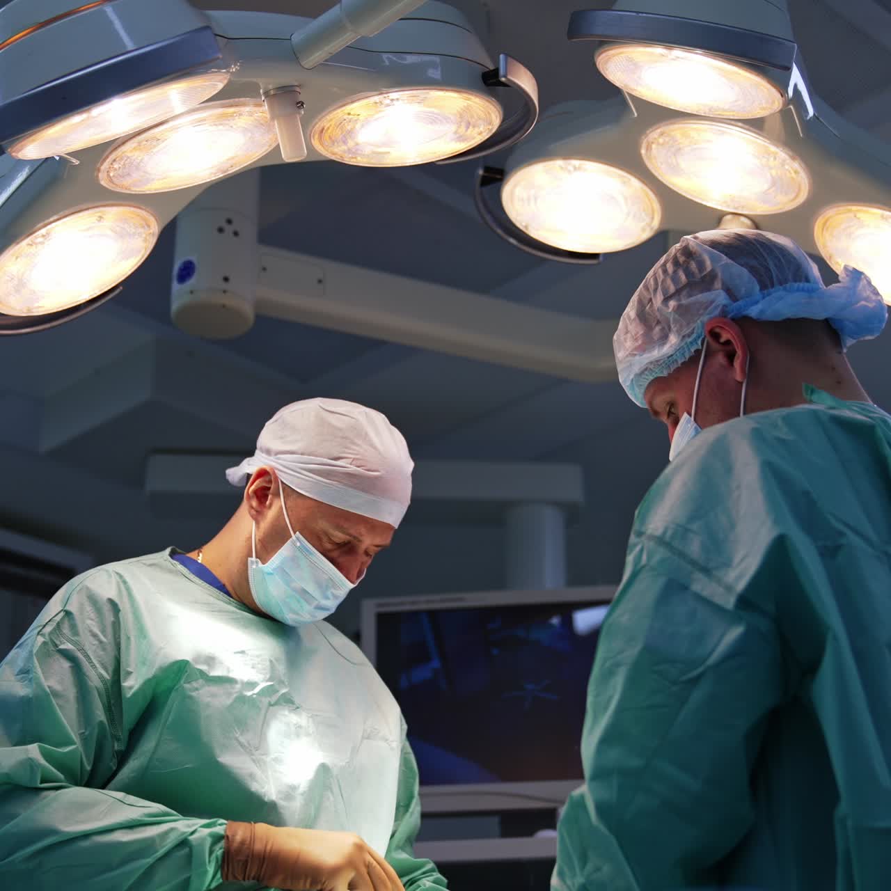 Two surgeons working under the bright lamps of surgery room. Chief doctor using the electric tool which is producing little smoke at usage