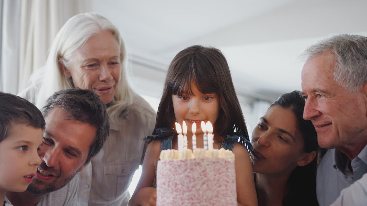 Famiglia multigenerazionale che festeggia un compleanno con la nipotina a casa mentre spegne le candeline.