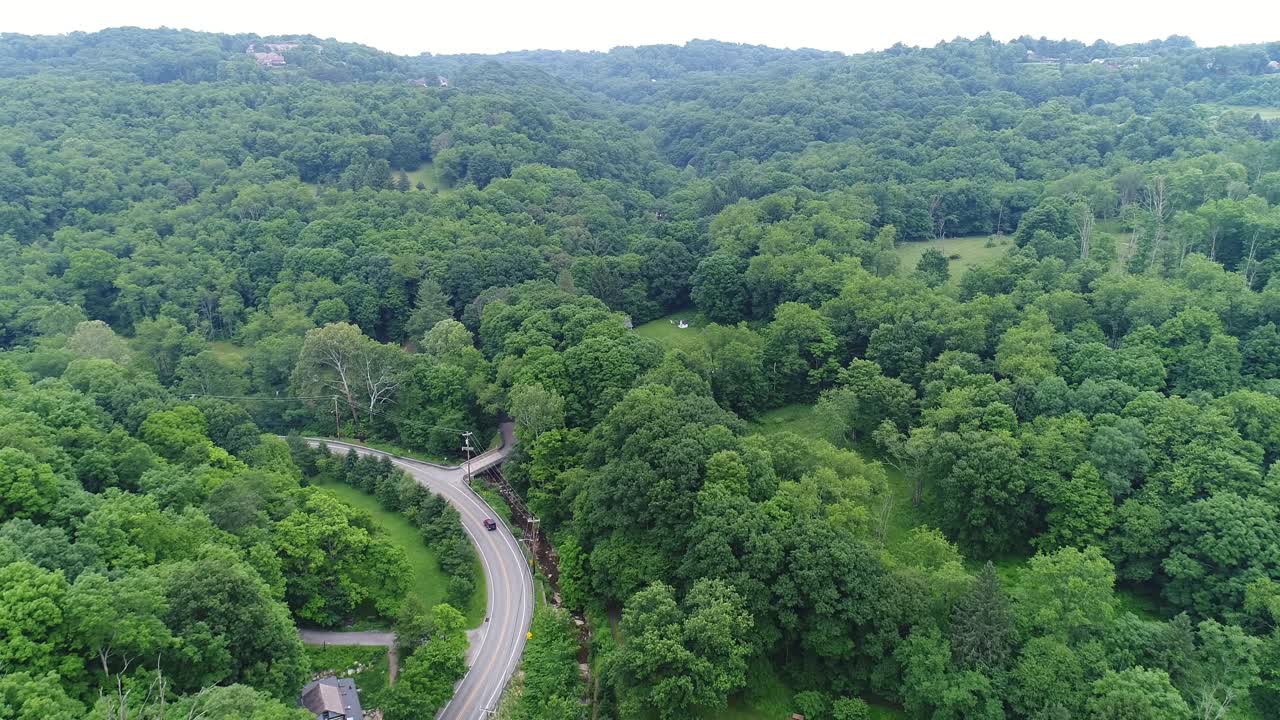 Aerial View of a Winding Road Through a Lush Green Forest Valley