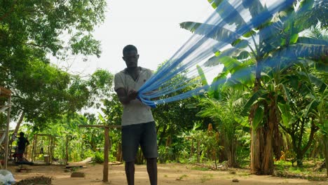 poor black man rolling up a blue kente cloth in a tropical village in ghana