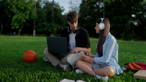 dos jóvenes sentados en un parque, hablando y trabajando en una computadora portátil
