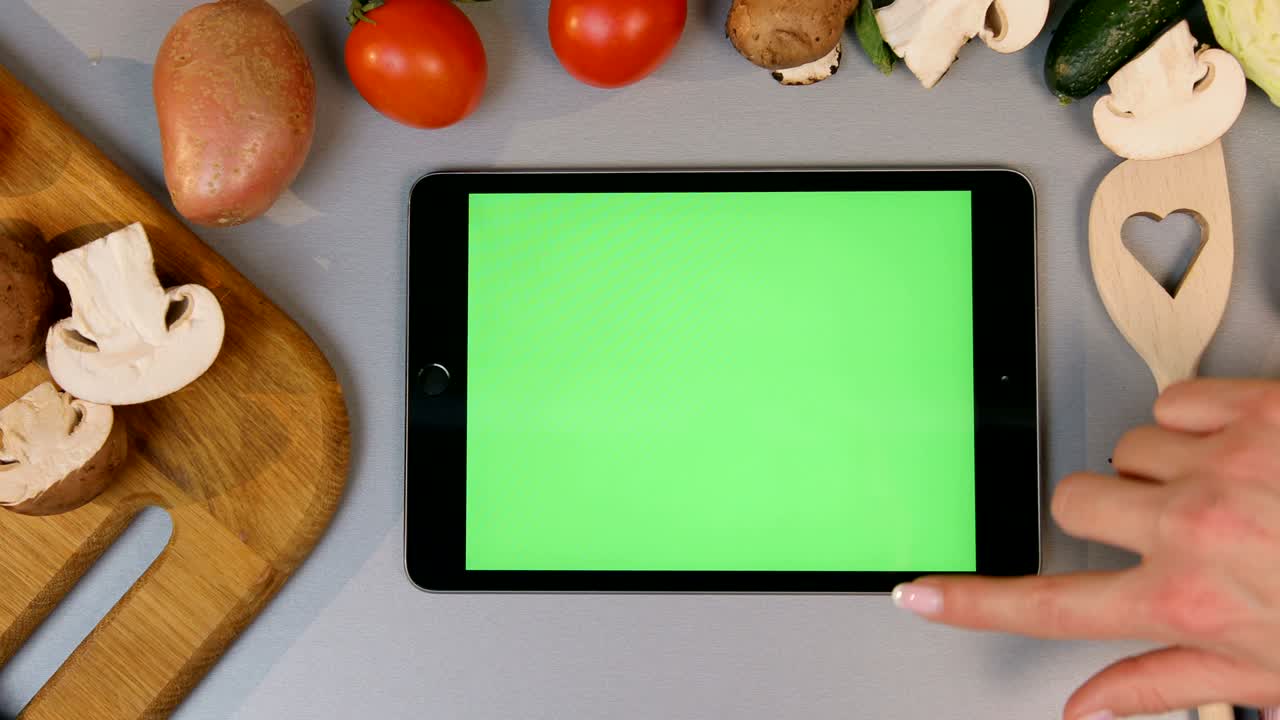 주방에서 스크롤하는 태블릿. 채소가 배경에 있습니다.