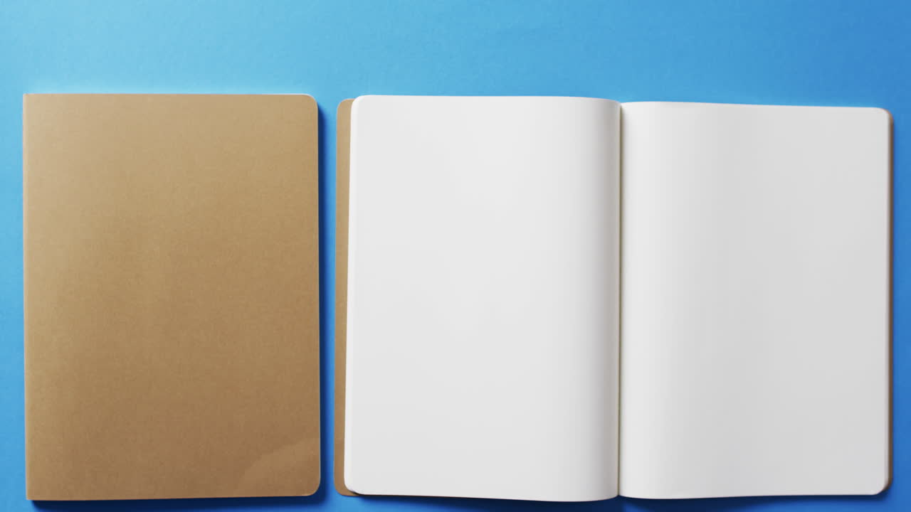Close up of open blank book and brown notebook with copy space on blue background in slow motion