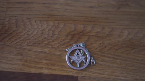 a pan over in different speeds of masonic freemason talisman necklace with g symbol sitting on wood table in 4k 60fps