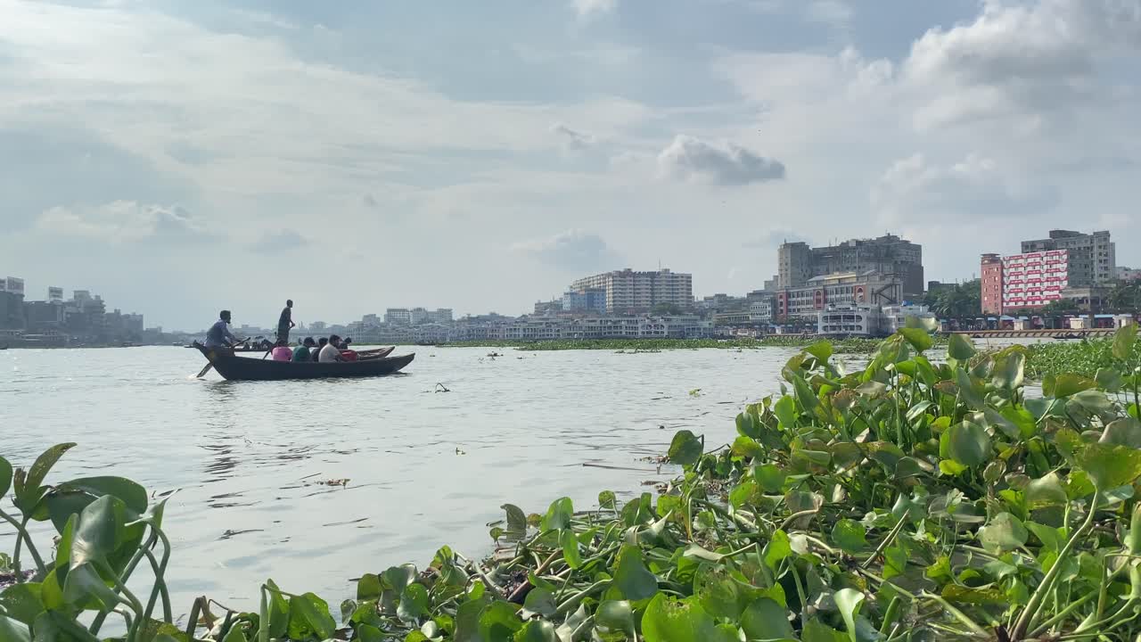 Tracking shot of men paddling a wooden boat through the river in Bangladesh