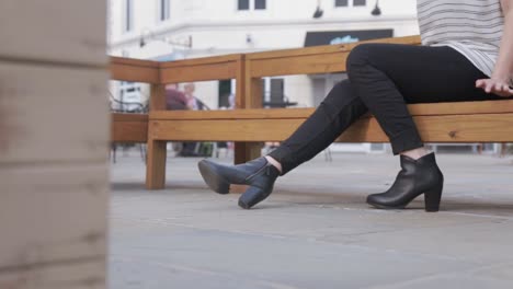 toma de diapositivas ambientada en un distrito de estilo francés de una mujer vestida con jeans negros y botas de moda de diseñador negras sentada en un banco de madera