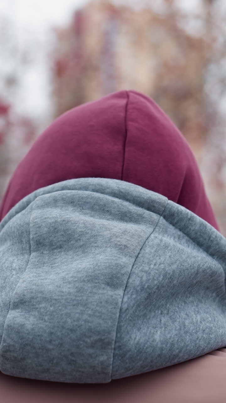 Vista ravvicinata posteriore di una persona che si sistema il berretto mentre cammina in un freddo parco invernale, terreno innevato, sfondo sfocato con alberi spogli e bacche rosse