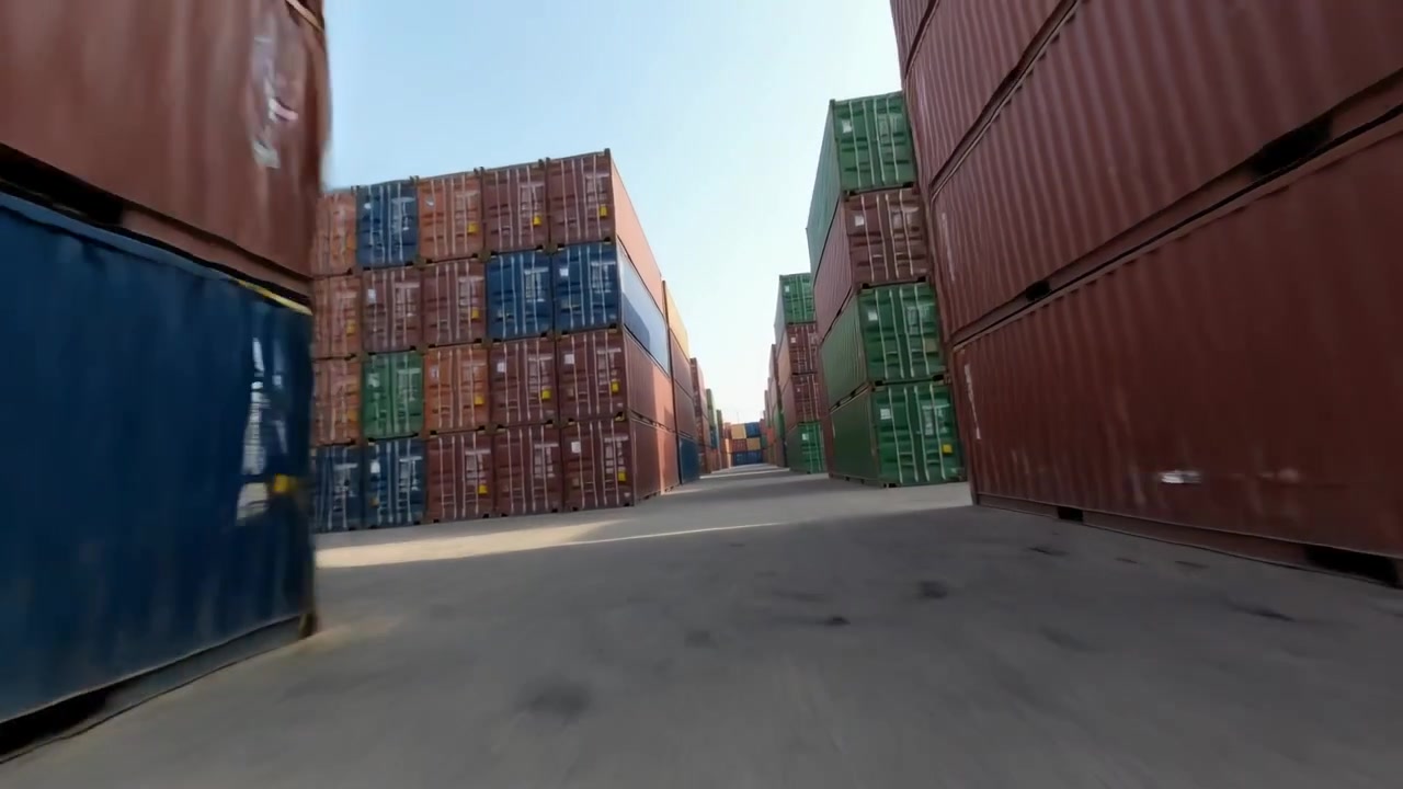 Telecamera in movimento che parte dall'imbocco del corridoio, percorre il piazzale, mostrando container colorati impilati