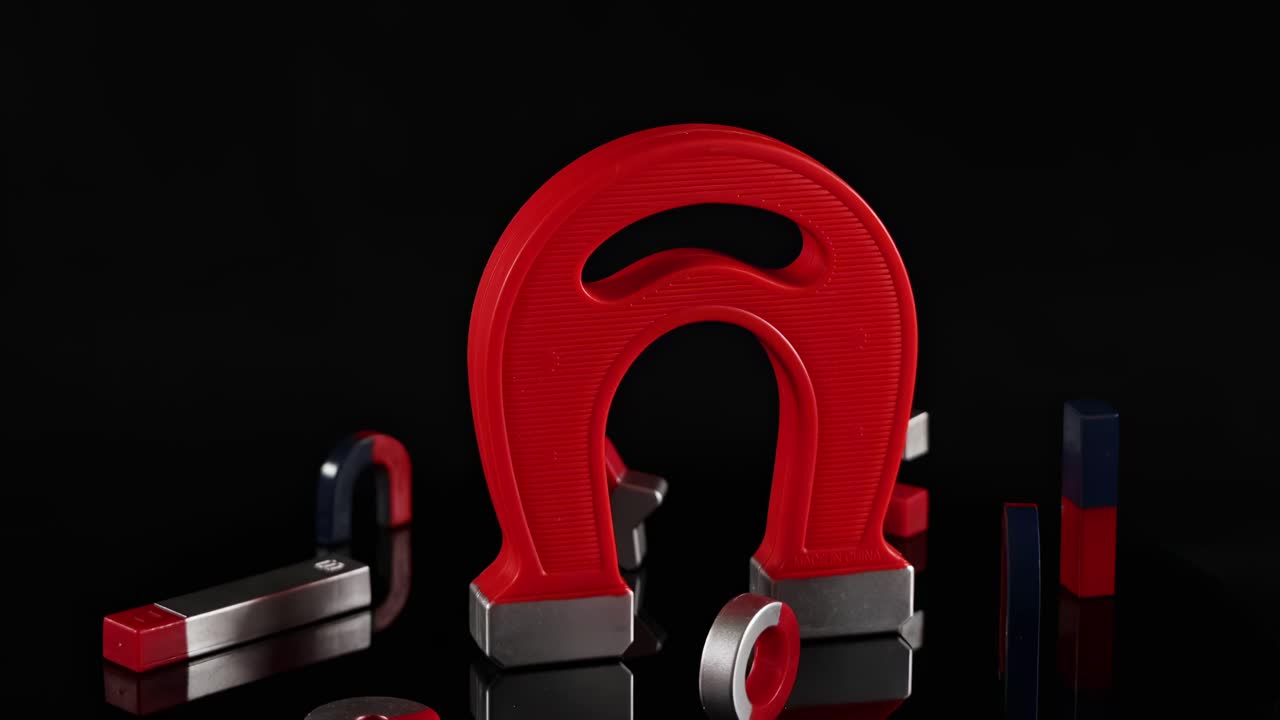 U-shaped and cylindrical magnets interact dynamically on a dark surface, showcasing magnetic forces and movement.