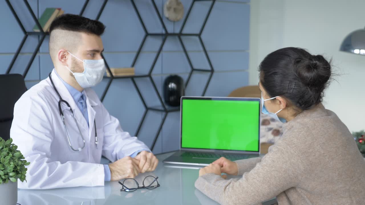 전문적인 남성 의사가 데이터를 채우고, 녹색 화면으로 컴퓨터에서 의료 보고서를 작성하고, 아름다운 성인 여성이 의사 에 앉아 병실에서 기다리고 있습니다.
