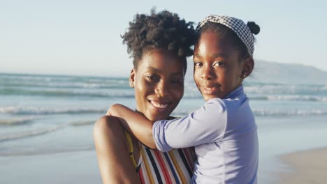 Porträt-Einer-Glücklichen-Afroamerikanischen-Mutter,-Die-Ihre-Tochter-Am-Sonnigen-Strand-Trägt