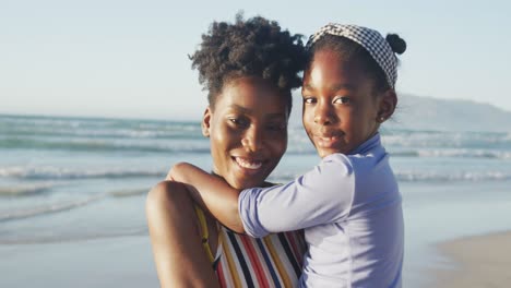 portrait of happy african american mother carrying daughter on sunny beach