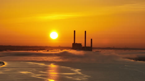 a long focal range drone shot, in lateral motion or side tracking, of a french coal power plant factory shut down , near the loire river, with mist and haze and fog, at sunrise