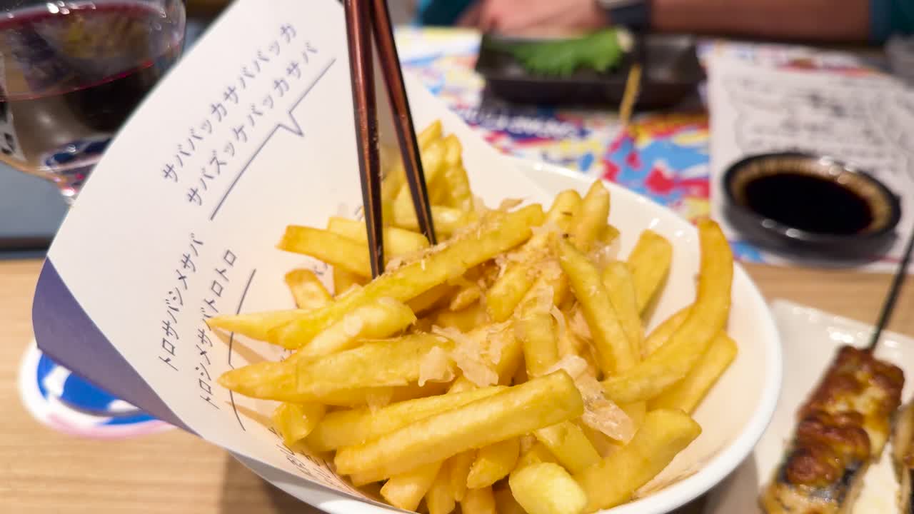 Close-up shot of chopsticks picking up fusion style french fries on a wooden table
