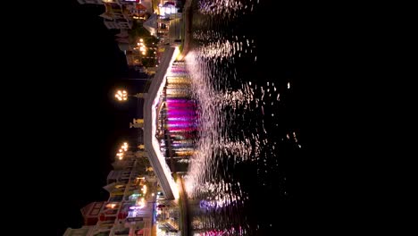 drone flying over the illuminating bridge tourist at boat sailing on phu quoc river at grand world at night in kien giang, vietnam. aerial, vertical shot