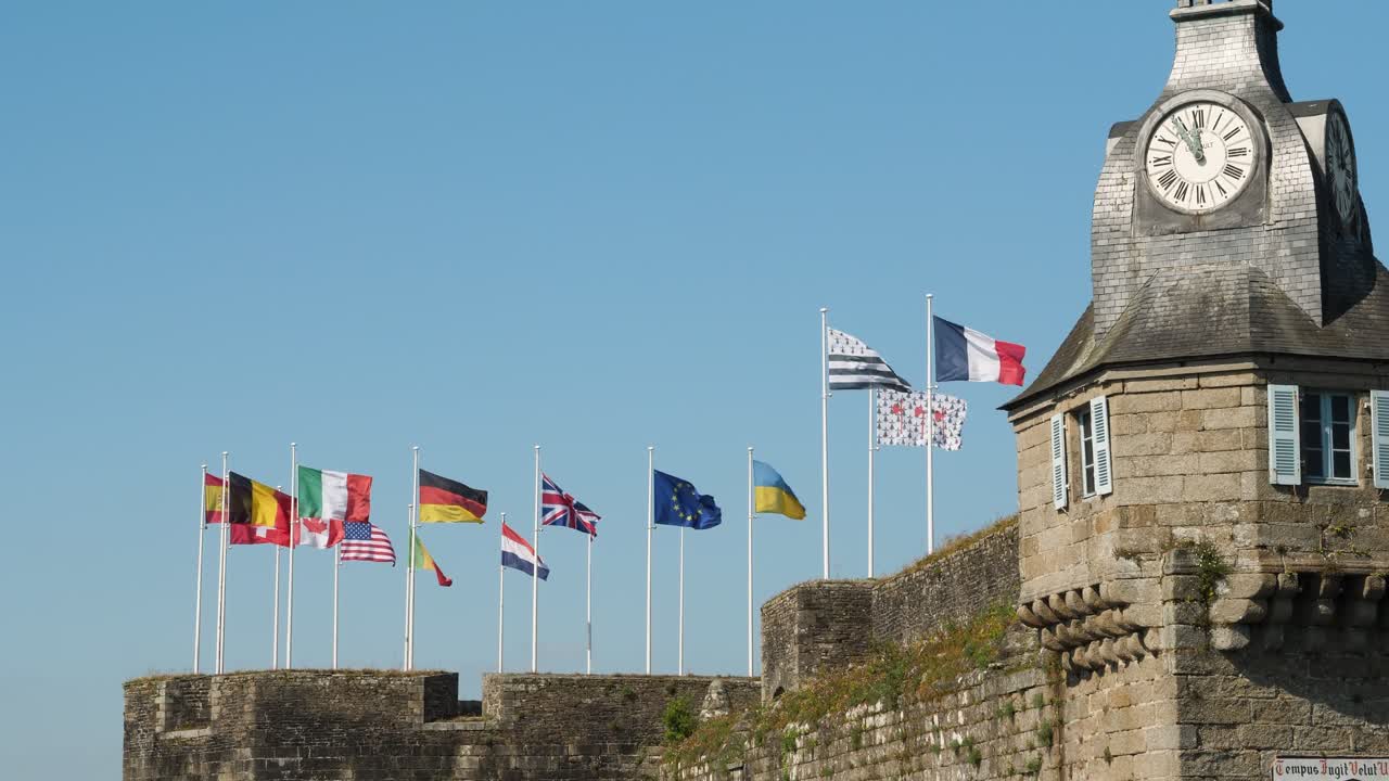 Static shot under clear blue sky, international flags fly over medieval stone ramparts of Concarneau's Ville Close, Brittany, France