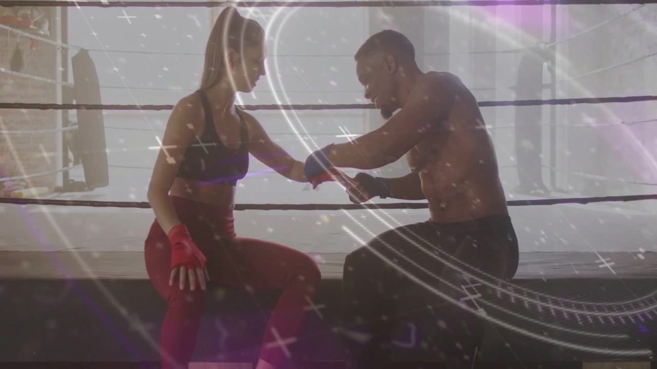 Female athlete extending arm, male trainer wrapping wrist and knuckles for boxing, sparkles passing