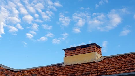 brick chimney on house roof and sparse clouds in blue sky simulating smoke