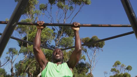 hombre afroamericano en forma haciendo ejercicio afuera, haciendo pull ups colgantes en un marco de escalada