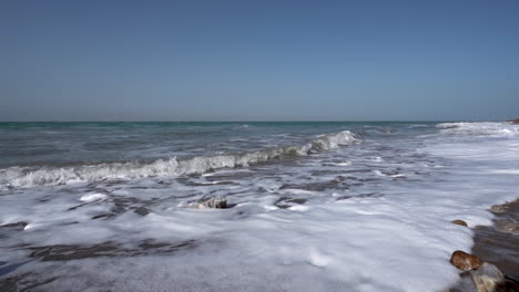 a dead sea shore on a clear sunny day with sea foam forming on a coast