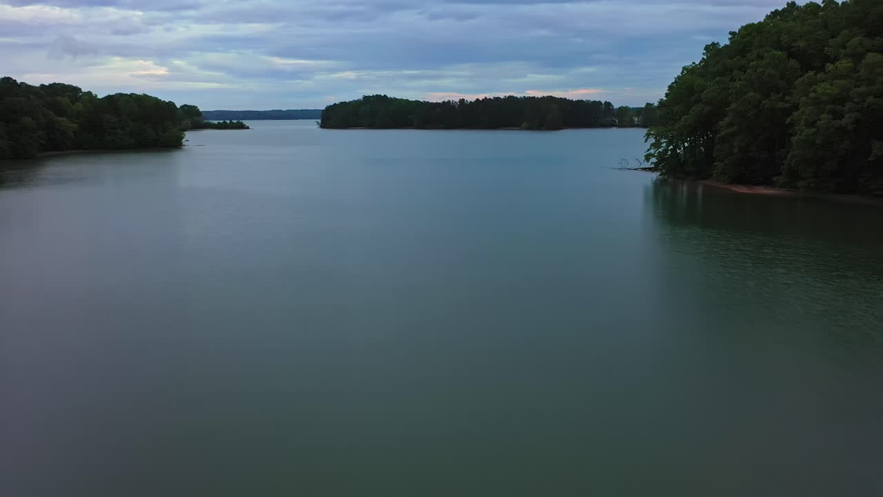 Slow drone flight over Lake Lanier with forest trees on shoreline during cloudy day. Georgia, America. Wide shot. Panorama shot.