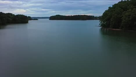 slow drone flight over lake lanier with forest trees on shoreline during cloudy day. georgia, america. wide shot. panorama shot.