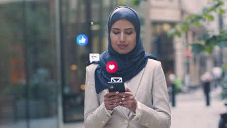 muslim businesswoman standing outside city offices looking at mobile phone with motion graphics emojis showing multiple networking messaging and social media notifications