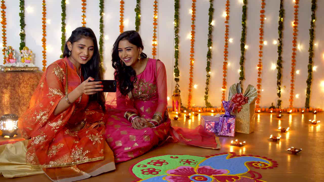 Two Indian sisters happily doing video call with a smartphone on Diwali festival