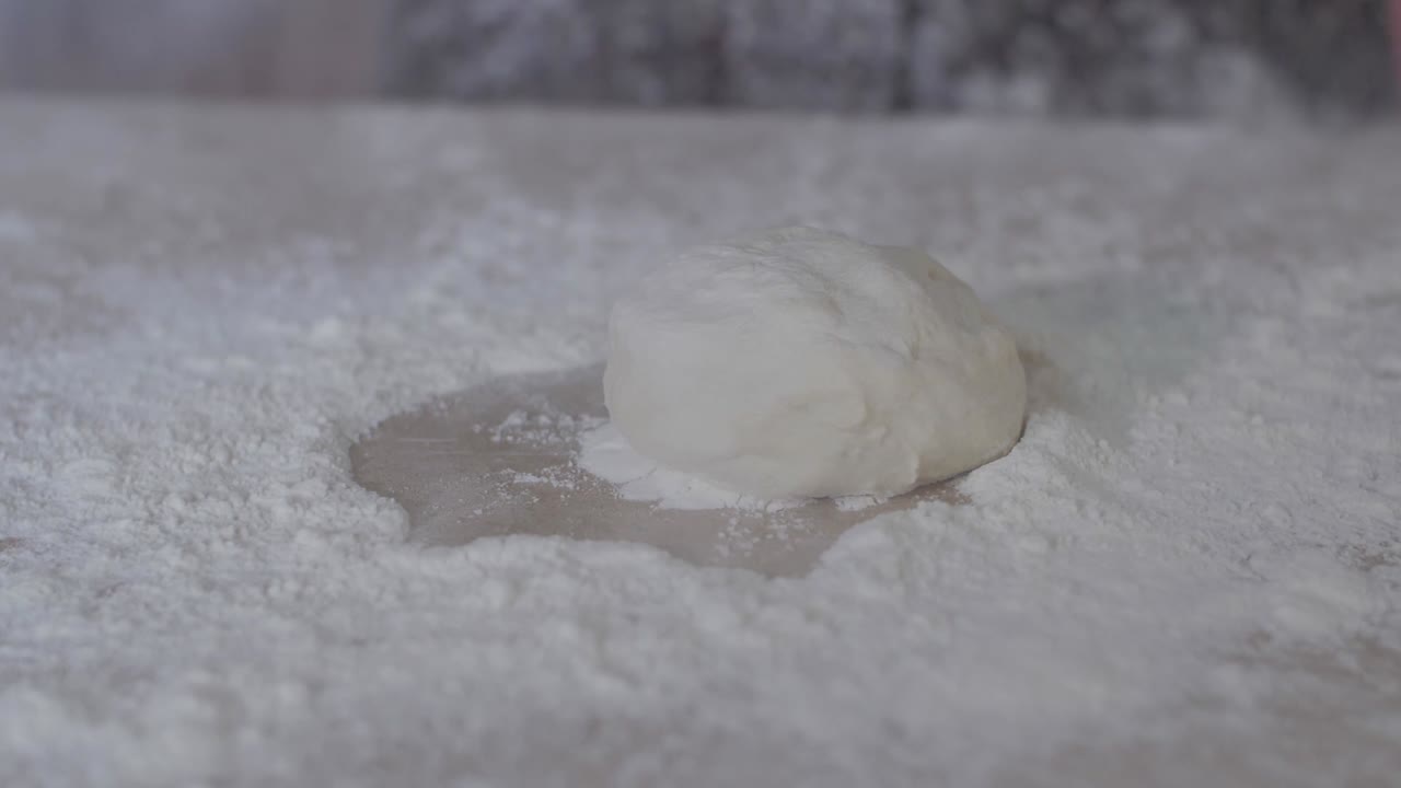 A ball of bread dough being dropped onto a floured surface creating a flour explosion from the side