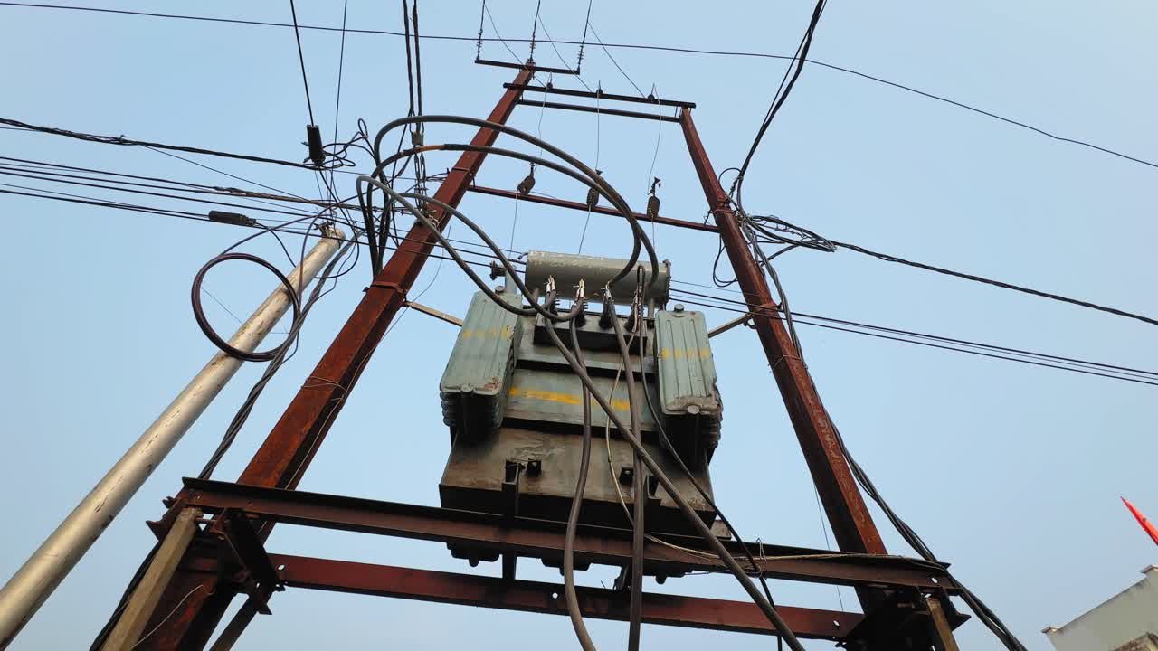 Camera orbiting around pole-mounted distribution transformer on H-type metal structure, showing connected cables, insulators and electrical hardware against clear sky background