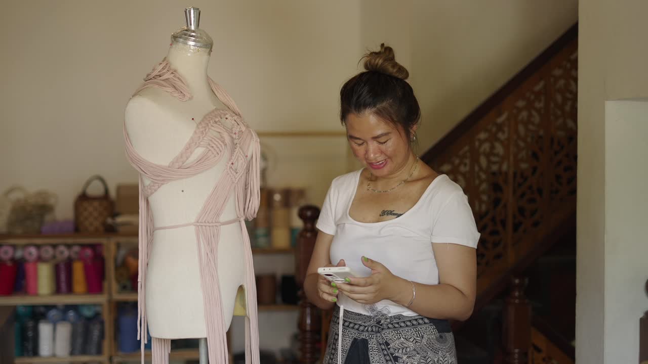 Woman crafting a macrame top in a creative studio while using her phone