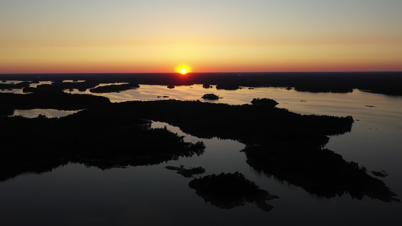 Aerial view over islands, in the Stockholm archipelago, during a colorful, summer sunset, at the Baltic sea, in Sweden - reverse, silhouette drone shot