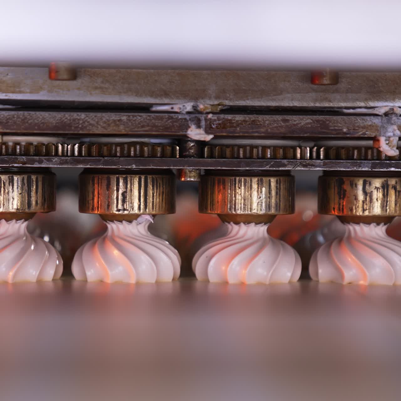 Metal rotating nozzles from automatic machine squeezing cream on conveyor. Vanilla marshmallow producing at factory. Close up