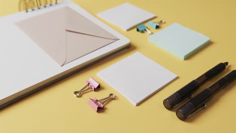 Flat-lay-of-pens,-envelope-and-memo-notes-with-copy-space-on-yellow-background