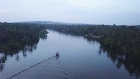 boat cruising in rippled backwaters of poovar with lush green vegetation and coconut trees lined up on the shores in kerala, india - aerial drone shot