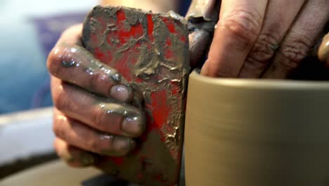 potters wheel with male ceramist shaping the edge of a tall vase with a guide tool, close up handheld shot