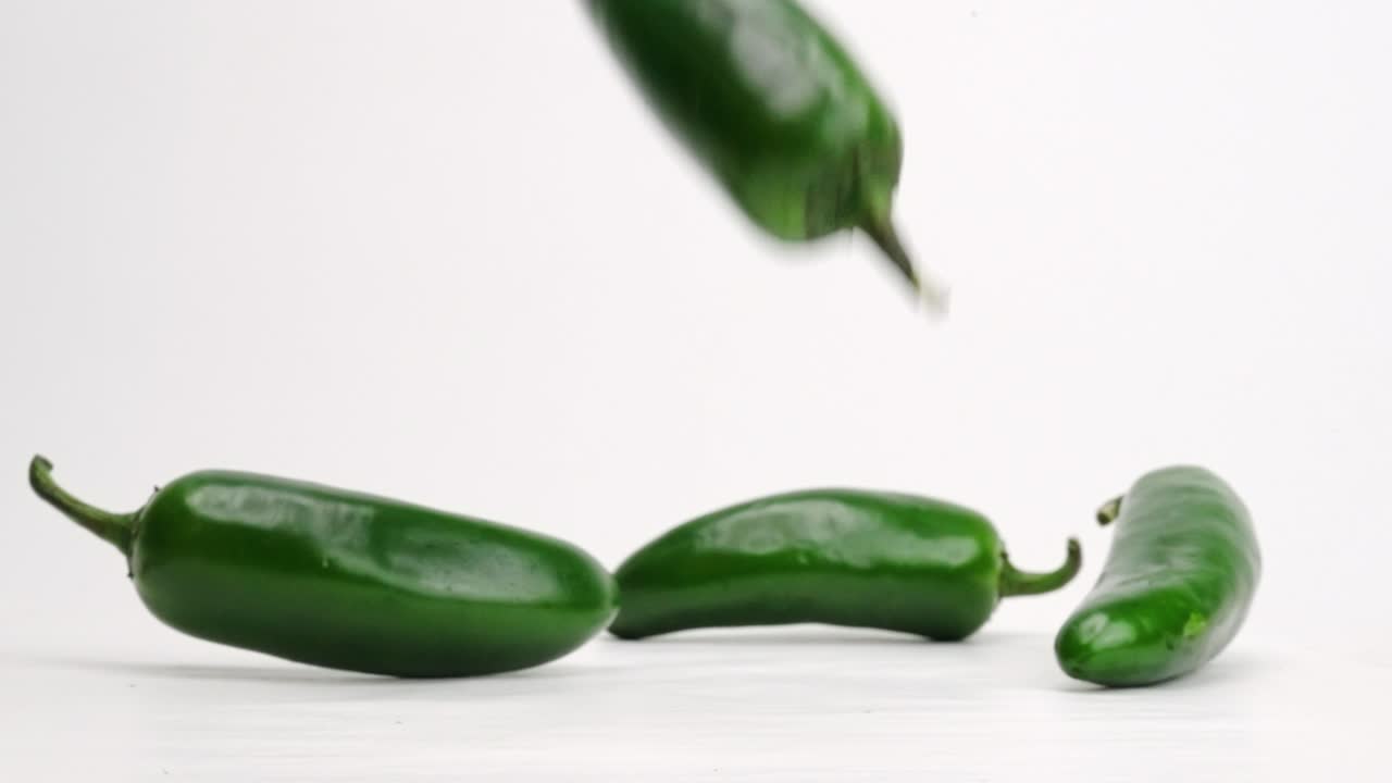 전체 녹색 jalapeños가 4k 느린 동작으로 흰색 스튜디오 배경에서 떨어지고 튀는