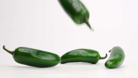 jalapeños verdes enteros cayendo y rebotando sobre fondo de estudio blanco en cámara lenta de 4k