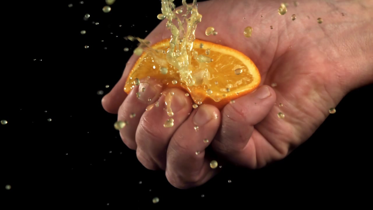 Mano exprimiendo media naranja fresca con salpicaduras de jugo