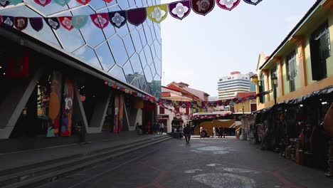 Camera tilts from festive paper flags to vibrant Little India street, bright daylight, urban reflections