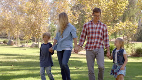 Junge-Weiße-Familie-Geht-Händchen-Haltend-In-Einem-Park-In-Der-Sonne-Spazieren