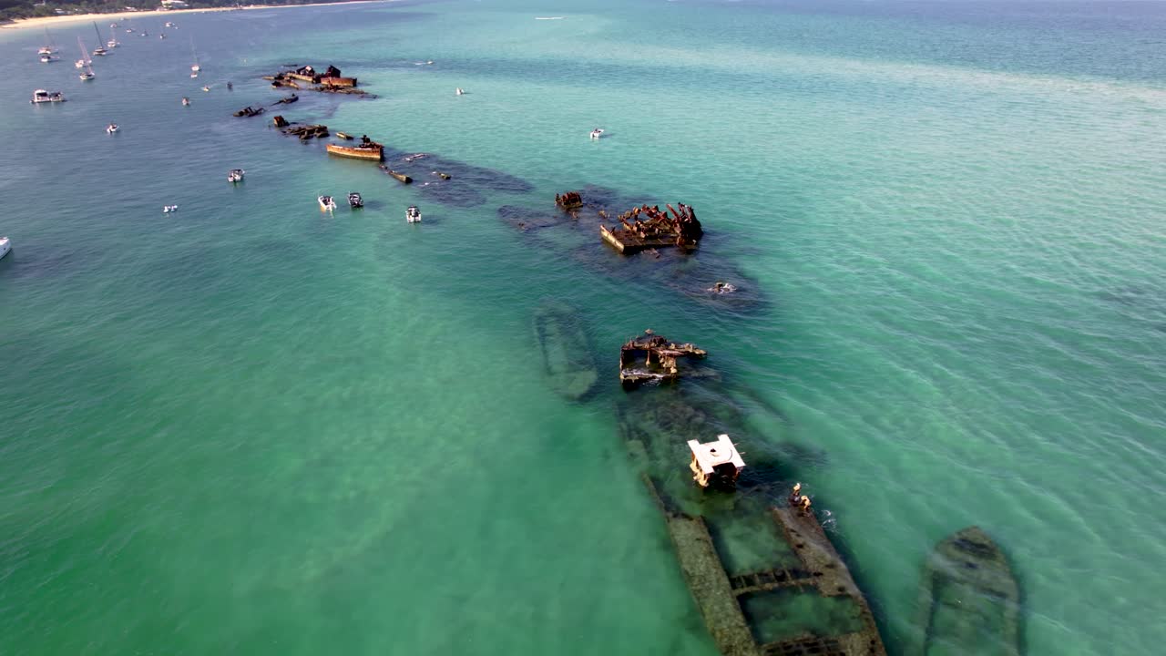 High aerial tracking right of Tangalooma Wrecks, showcasing turquoise water, reefs, and historic shipwrecks with dive boats guiding tourists