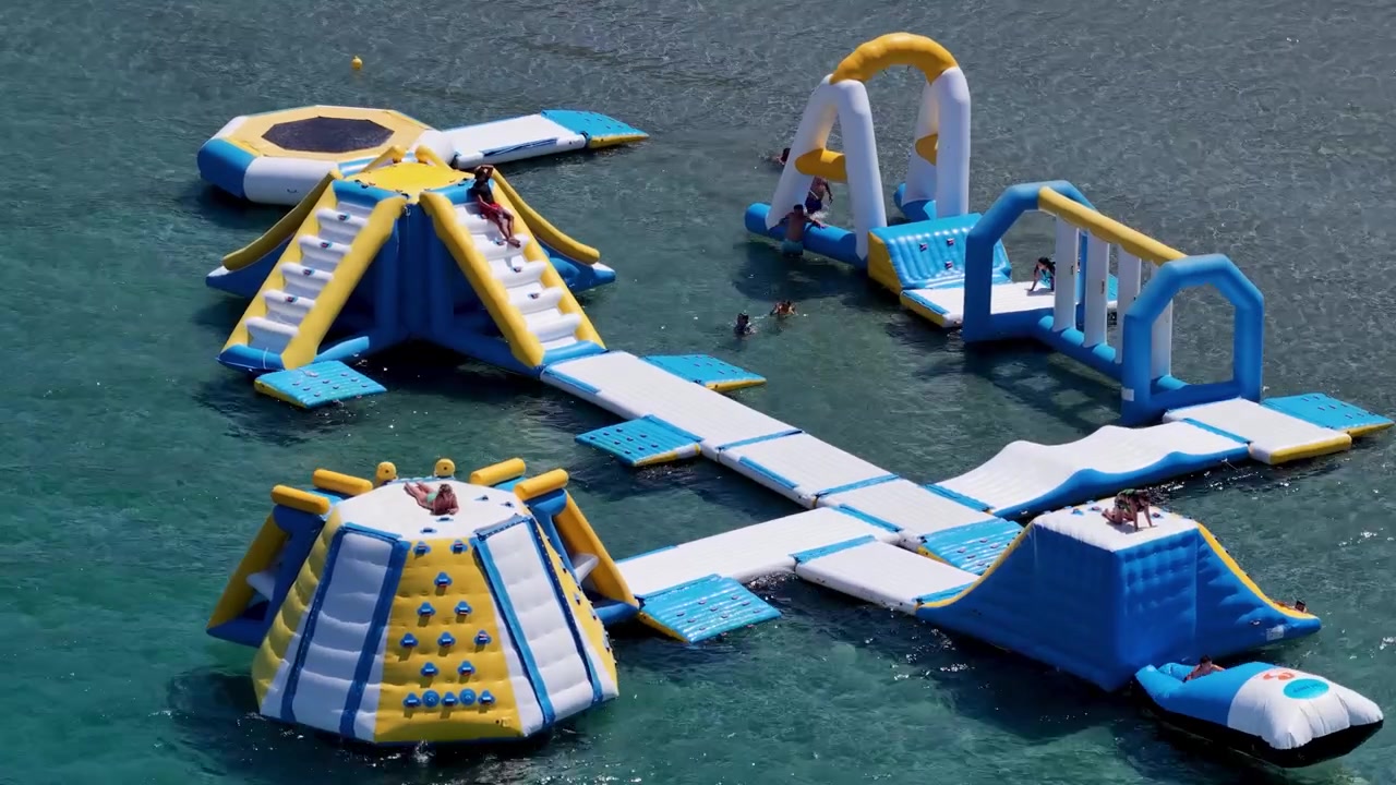 Drone flight over Kalamaki Apraos Beach and floating water park with lush green coastline in North Corfu, Greece