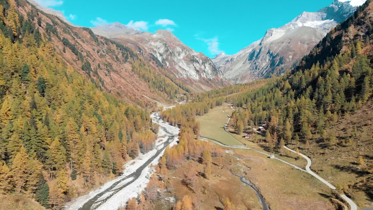a drone shot of a valley in the Austrian Alps, with a road and a river in the middle, surrounded by trees