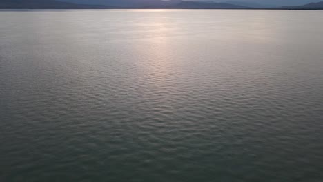 scenic utah lake water rippling on surface with mountain range in background at sunset, overhead aerial tilt up