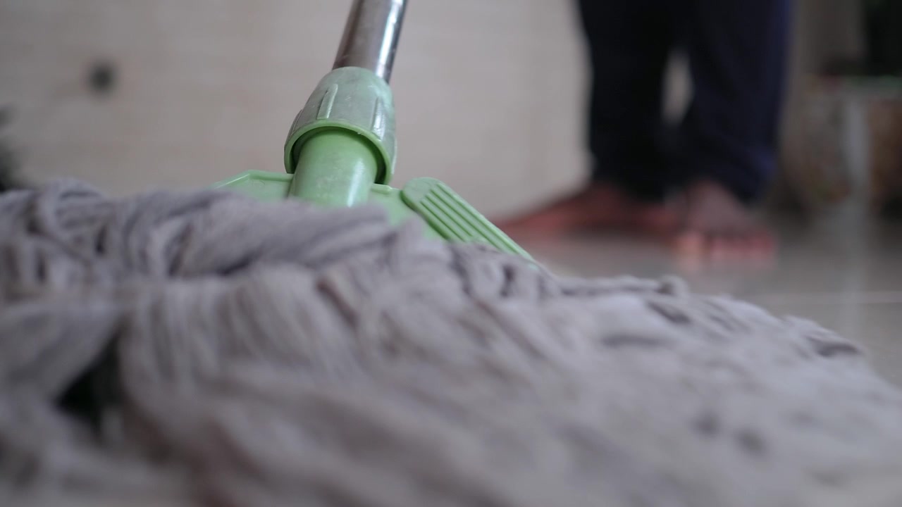 Osoba vytírající dlážděnou podlahu doma