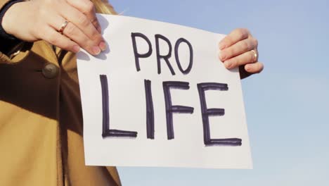 female holding pro life board against blue sky, close up view