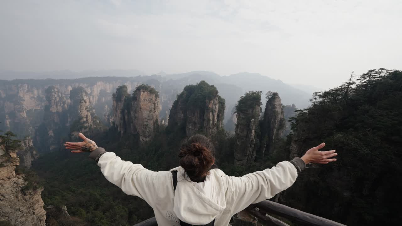 Person stretches arms wide facing the majestic stone pillars and forested peaks of Zhangjiajie in a moment of awe and connection