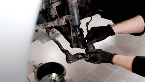 close up of hands removing a suspension part of a car after hammering it loose. static shot in 4k.