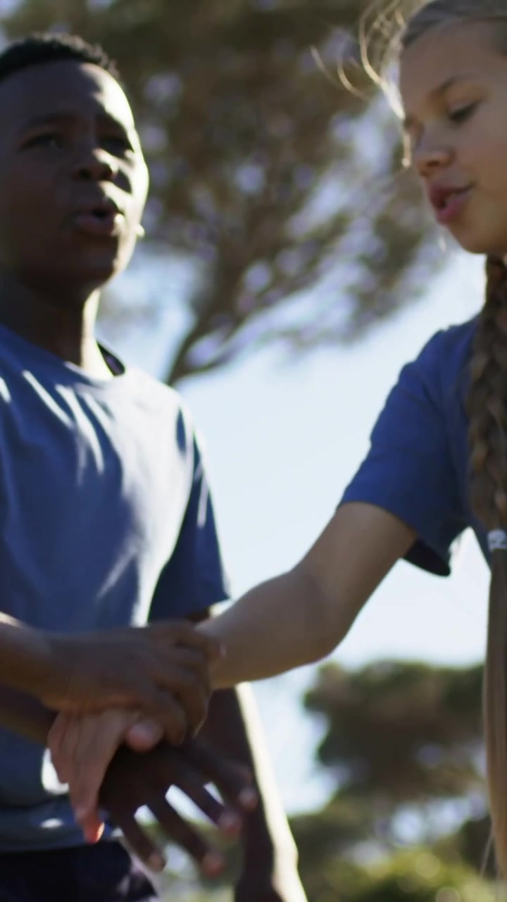 Vertical video: Offering hand in park, boy urging braided girl in blue tee to greet, clips